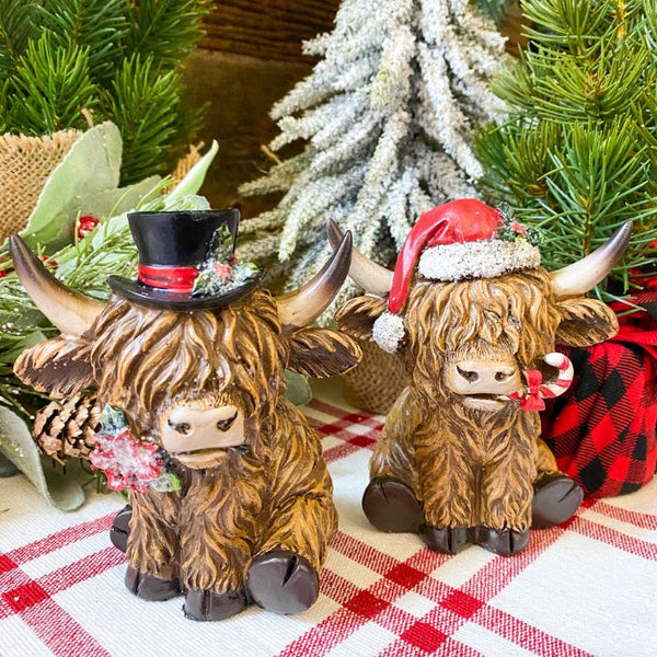 Christmas Highland Cow Figurines - Two Styles are ready for Christmas with their hats - one with a top hat and the other a red Santa Hat. Available at Quilted Cabin Home Decor.