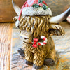 Christmas Highland Cow Figurines - Two Styles are ready for Christmas with their hats - one with a top hat and the other a red Santa Hat. Available at Quilted Cabin Home Decor.