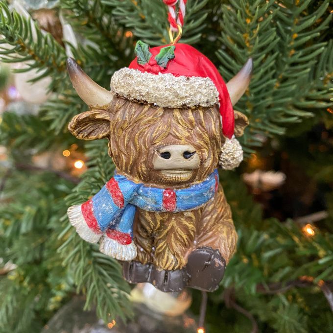 highland cow ornament with a red hat and blue scarf hanging on a Christmas tree. Highland Cow Ornaments - Three Styles available at Quilted Cabin Home Decor.