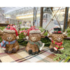 Three decorative Highland cow figurines wearing festive hats and scarves on a checkered surface. Highland Cow Ornaments - Three Styles available at Quilted Cabin Home Decor.