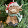 Decorative Highland cow ornament with a Santa hat and green scarf on a Christmas tree. Highland Cow Ornaments - Three Styles available at Quilted Cabin Home Decor.