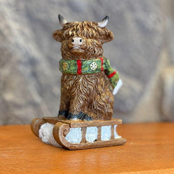 Highland Cow with green scarf on sled ornament available at Quilted Cabin in Airdrie