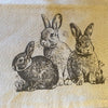 Illustration of three rabbits on a textured fabric background. Baby Bunny Trio Table Runner available at Quilted Cabin Home Decor.