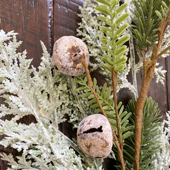 Artificial greenery with frosted jingle bells against a wooden background.  Frosted Cedar & Pine Spray - 30" tall available at Quilted Cabin Home Decor.