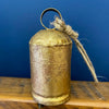 Vintage-style gold bell with a rope on a wooden surface against a blue wall. Gold Clapper Bells - Three Sizes available at Quilted Cabin Home Decor.