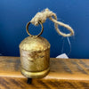 Gold bell with a rope on a wooden surface against a blue wall. Gold Clapper Bells - Three Sizes available at Quilted Cabin Home Decor.