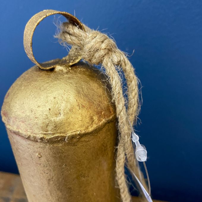 Gold bell with a jute string against a blue background. Gold Clapper Bells - Three Sizes available at Quilted Cabin Home Decor.