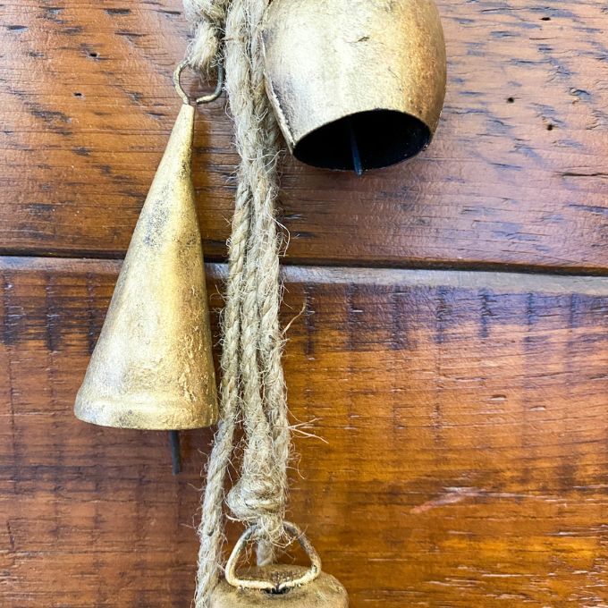 Two rustic gold bells hanging on a wooden surface. Mixed Gold Bells Hanger available at Quilted Cabin Home Decor.