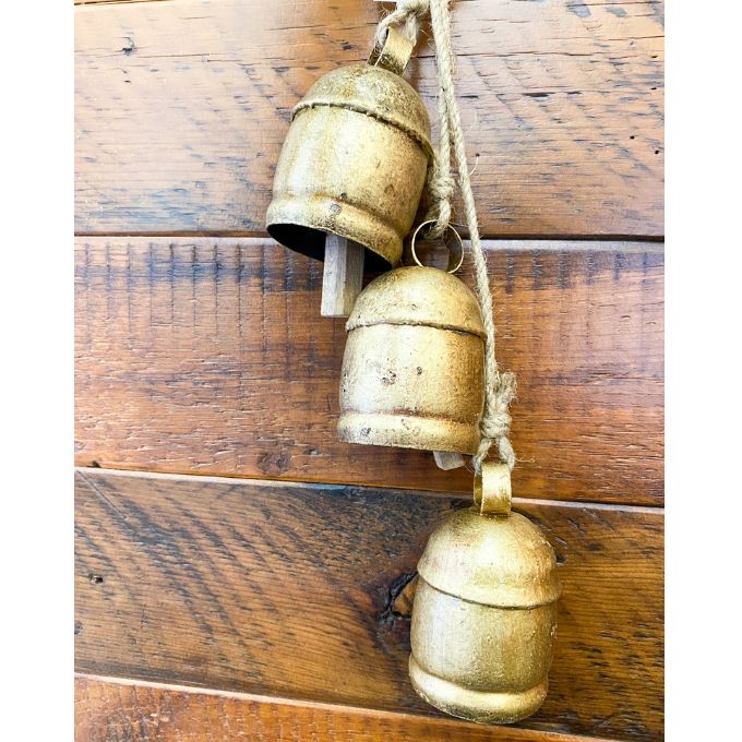 Three vintage gold bells hanging on a wooden wall. Three Gold Clapper Bell Hanger available at Quilted Cabin Home Decor.