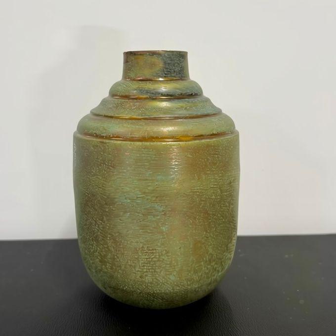 A small ceramic vase with a rounded body and a tiered neck, featuring a textured metallic finish in olive green, bronze, and gold tones, set against a plain white background.