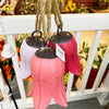 Pink and white wind chimes hanging on a white railing with a blurred floral background. Tulip Bells - Three Colours available at Quilted Cabin Home Decor.
