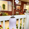 Decorative white tulip bell hanging on a porch with flowers. Tulip Bells - Three Colours available at Quilted Cabin Home Decor.