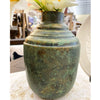 Green metal vase with floral arrangement on a textured surface. Rustic Patina Metal Vase  available at Quilted Cabin Home Decor.