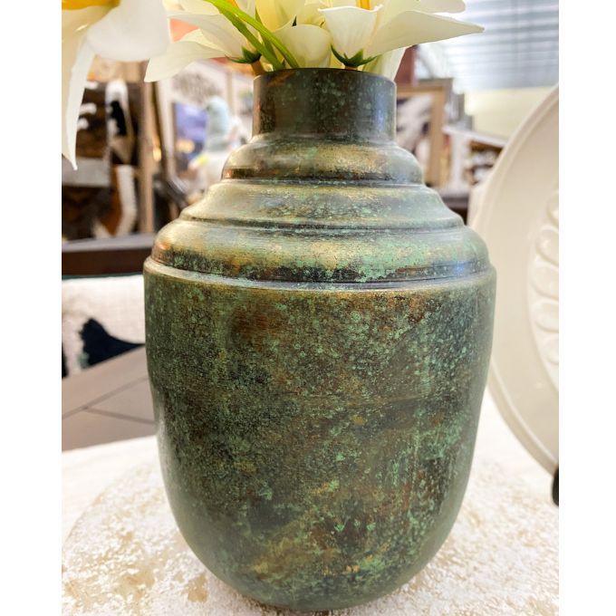 Green metal vase with floral arrangement on a textured surface. Rustic Patina Metal Vase  available at Quilted Cabin Home Decor.