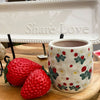 Decorative strawberries and a strawberry-patterned planter with a white plate labeled 'Share Love' on a wooden surface. Resin Strawberries - Set of Two available at Quilted Cabin Home Decor.