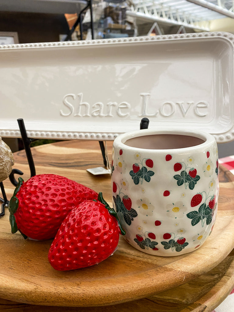 Ceramic planter with strawberry pattern on a wooden surface, next to decorative strawberries. Resin Strawberries - Set of Two available at Quilted Cabin Home Decor.