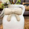 White vase with a beige bow and plant on a wooden surface. Bow Pot Hangers - Three Colours available at Quilted Cabin Home Decor.