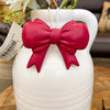 White vase with a red bow and floral arrangement on a wooden surface. Bow Pot Hangers - Three Colours available at Quilted Cabin Home Decor.