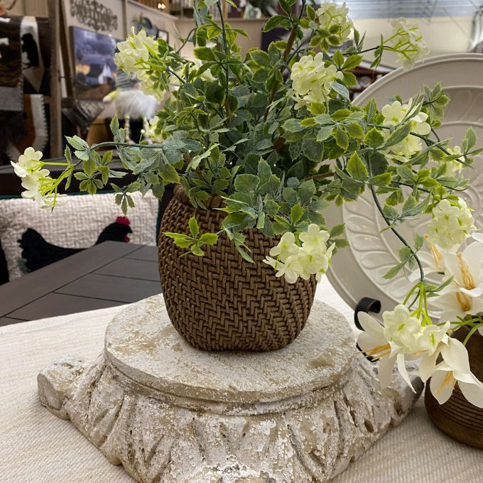 Decorative table setting with artificial plants in woven baskets on a textured surface. Rattan Look Resin Vase available at Quilted Cabin Home Decor.