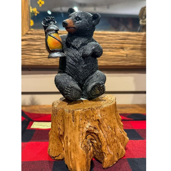 Bear figurine holding a lantern on a wooden stump with a checkered cloth background.  Tree Trunk Riser is available at Quilted Cabin home decor.