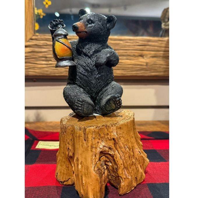 Bear figurine holding a lantern on a wooden stump with a checkered cloth background.  Tree Trunk Riser is available at Quilted Cabin home decor.