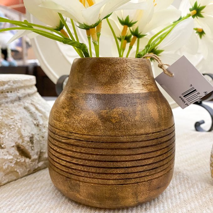 Wooden textured vase with a tag on a surface with flowers in the background. Distressed Round Wooden Vases - Two Sizes available at Quilted Cabin Home Decor. 