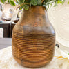 Wooden vase with a textured surface holding greenery on a light-colored surface. Distressed Round Wooden Vases - Two Sizes available at Quilted Cabin Home Decor. 