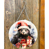 Decorative circular sign with a bear wearing a Santa hat and presents on a wooden background. Christmas Bear Round Wall Hanger available at Quilted Cabin Home Decor.