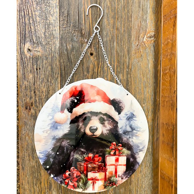 Decorative circular sign with a bear wearing a Santa hat and presents on a wooden background. Christmas Bear Round Wall Hanger available at Quilted Cabin Home Decor.