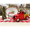 Red vintage truck on a checkered tablecloth with Christmas decorations in a store setting. Pine Christmas Tree Figurine available at Quilted Cabin Home Decor.