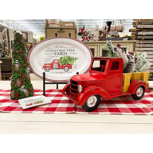 Red vintage truck on a checkered tablecloth with Christmas decorations in a store setting. Pine Christmas Tree Figurine available at Quilted Cabin Home Decor.