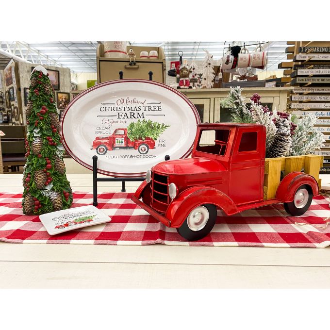 Red vintage truck on a checkered tablecloth with Christmas decorations in a store setting. Pine Christmas Tree Figurine available at Quilted Cabin Home Decor.
