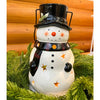 Snowman-shaped lantern with a top hat and star decorations on a green background. Snowman Lantern available at Quilted Cabin Home Decor.