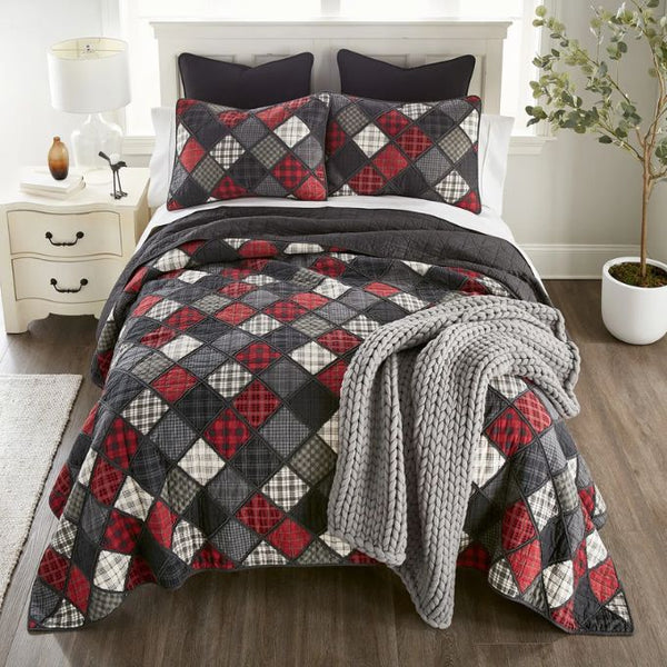 Bed with patchwork quilt and gray throw blanket in a bedroom setting. Lumberjack King Quilt Set available at Quilted Cabin Home Decor.