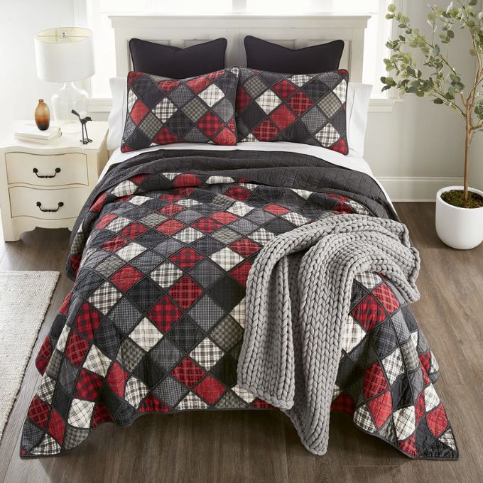 Bed with patchwork quilt and gray throw blanket in a bedroom setting. Lumberjack King Quilt Set available at Quilted Cabin Home Decor.