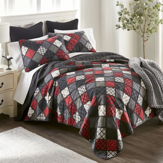 Quilted bedspread with red, gray, and black diamond pattern on a bed in a bedroom setting. Lumberjack King Quilt Set available at Quilted Cabin Home Decor.