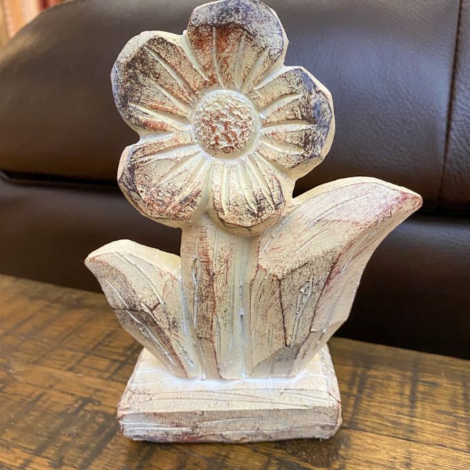Decorative flower figurine on a wooden surface with a brown leather couch in the background. Woodgrain Stoneware Flower Figurine available at Quilted Cabin Home Decor.