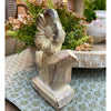 Decorative stone flower figurine on a table with plants in the background. Woodgrain Stoneware Flower Figurine available at Quilted Cabin Home Decor.