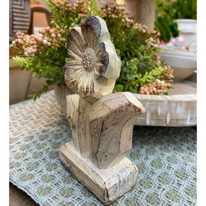 Decorative stone flower figurine on a table with plants in the background. Woodgrain Stoneware Flower Figurine available at Quilted Cabin Home Decor.
