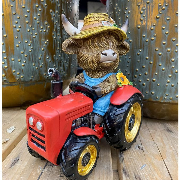Toy figure of a highland cow in a garden hat driving a red tractor against a metallic background. Highland Cow Tractor Figurine available at Quilted Cabin Home Decor.