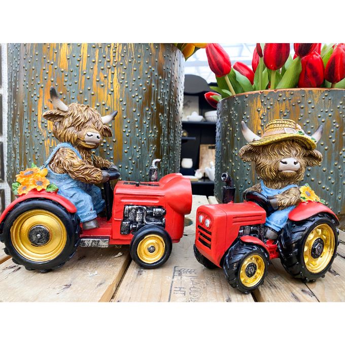 Two toy tractors figurines with Highland cow figures on a wooden surface, next to a pot of red tulips. Highland Cow Tractor Figurine available at Quilted Cabin Home Decor.