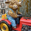 Figurine of a cow in overalls driving a red tractor with a sunflower decoration. Highland Cow Tractor Solar Figurine available at Quilted Cabin Home Decor.