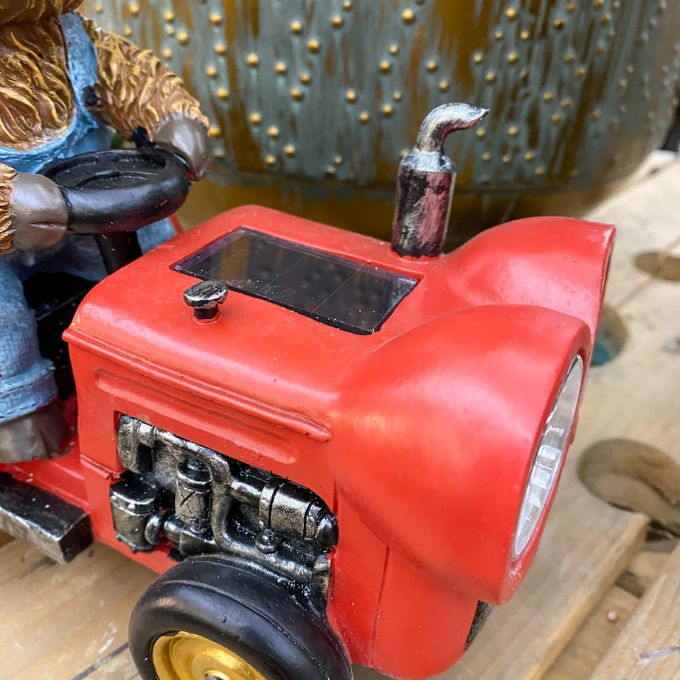 Red tractor figurine on a wooden surface. Highland Cow Tractor Solar Figurine available at Quilted Cabin Home Decor.