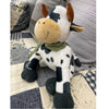 Plush cow toy on a patterned fabric background.  Moo Cow Stuffie available at Quilted Cabin Home Decor.