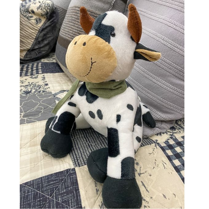 Plush cow toy on a patterned fabric background.  Moo Cow Stuffie available at Quilted Cabin Home Decor.