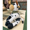 Plush cow toy on a patterned surface with a rustic background.  Moo Cow Stuffie available at Quilted Cabin Home Decor.