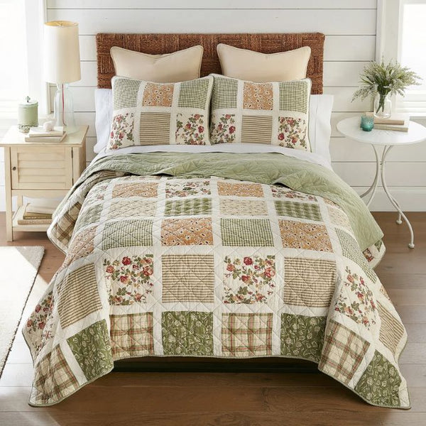 Patchwork quilt with floral patterns on a bed in a bedroom setting. Peach Rose Quilt Set available at Quilted Cabin Home Decor.
