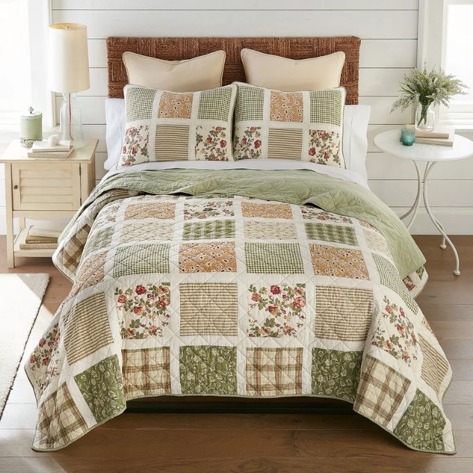 Patchwork quilt with floral patterns on a bed in a bedroom setting. Peach Rose Quilt Set available at Quilted Cabin Home Decor.