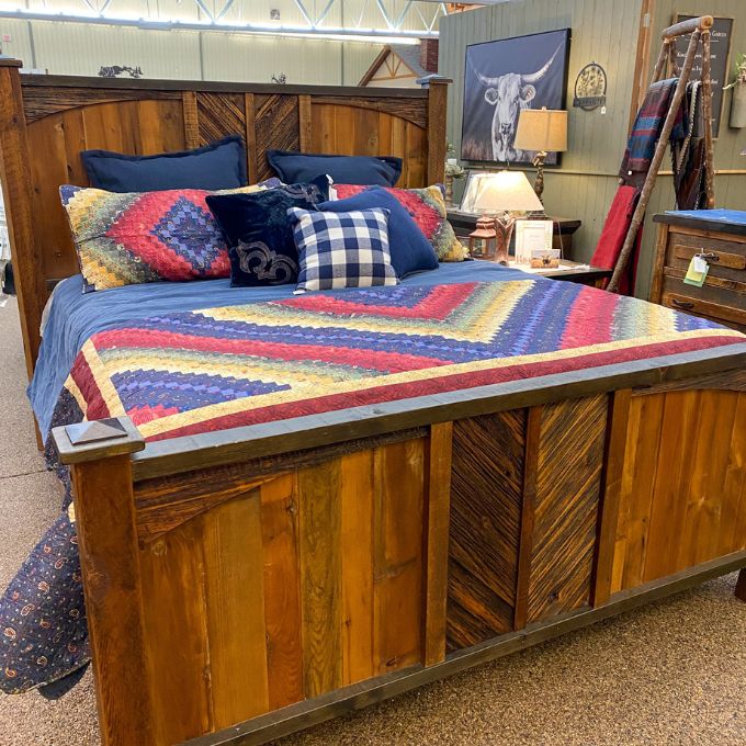 Wooden bed with colorful quilt and pillows in a store setting. Chesapeake King Quilt Set available at Quilted Cabin Home Decor.