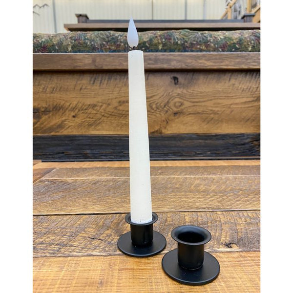 White candle in a black holder on wooden table. Small Round Taper Holder available at Quilted Cabin Home Decor.